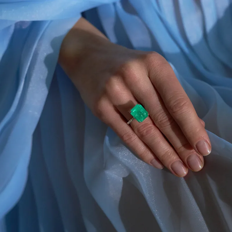 A hand with an emerald ring on blue pleated fabric