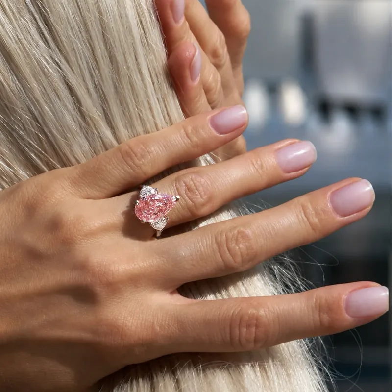 A hand with a pink diamond ring resting on blonde hair